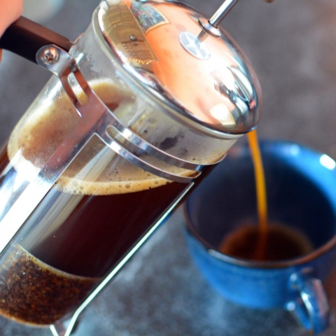 Coffee pours from a french press into a blue mug