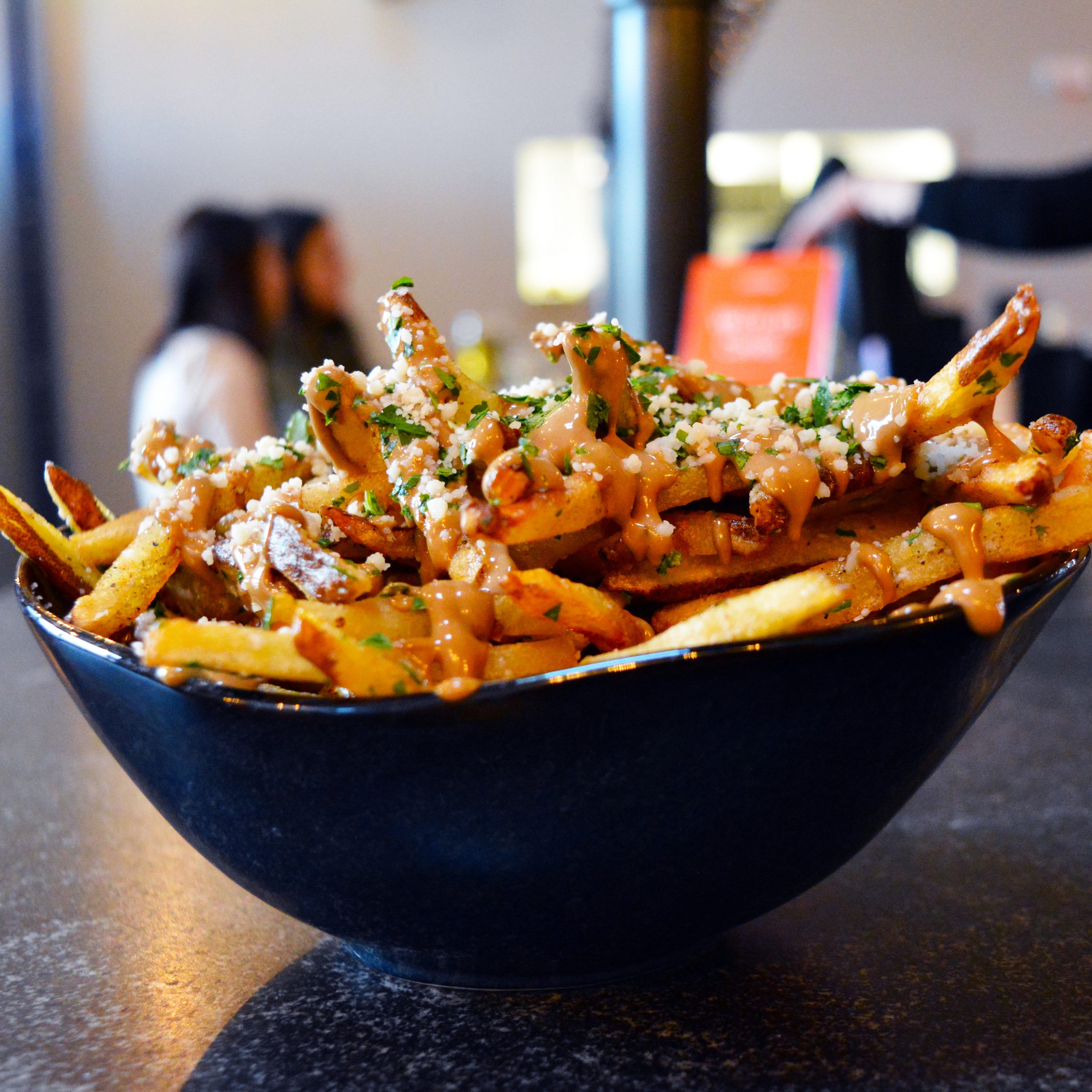 A photo of a bowl of fries, tossed in bone marrow, and topped with black garlic aioli